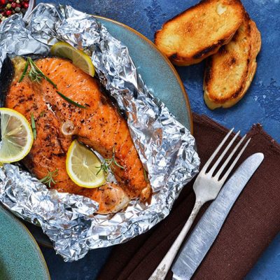 Baked in a foil steak salmon with a lemon and a marble on a wooden background.