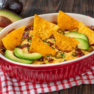 Jalapeno cheese dip in red casserole dish with nachos and avocado slices
