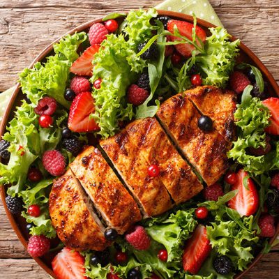 Sliced grilled chicken on lettuce with summer berries on brown plate