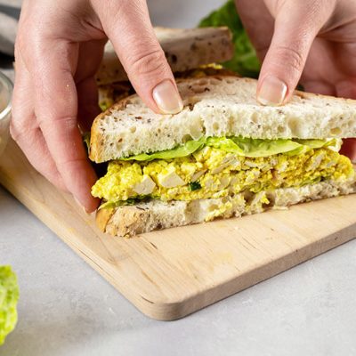 Hand holding egg salad sandwich with lettuce