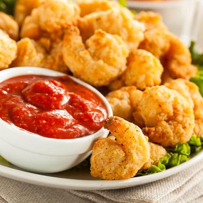 Pile of breaded shrimp on top of lettuce on white plate with cocktail sauce