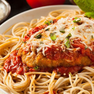 Italian chicken parmesan on top of noodles on white plate