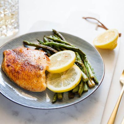 Baked tilapia served with asparagus stalks and lime slices on blue plate