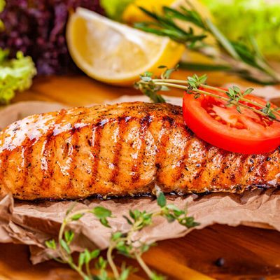 Grilled salmon topped with slice of tomato and herbs on wood board