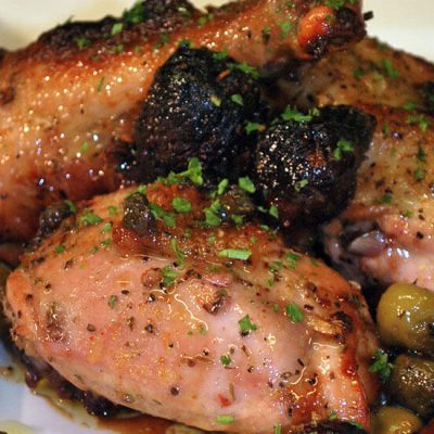 Chicken marbella with olives sprinkled with chopped herbs on plate
