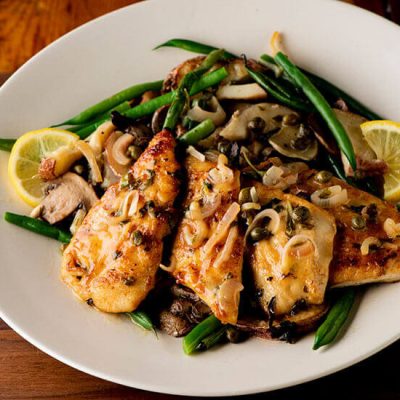 Chicken piccata with green beans and lemon slices on plate on wood counter