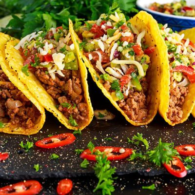 Five tacos with ground beef topped with shredded cheese on black counter