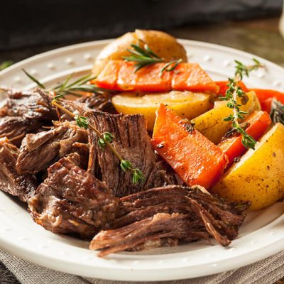 Slow cooked pot roast with carrots and potatoes on white plate on wood table