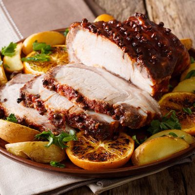 Half carved pork tenderloin surrounded by apple and orange slices on platter