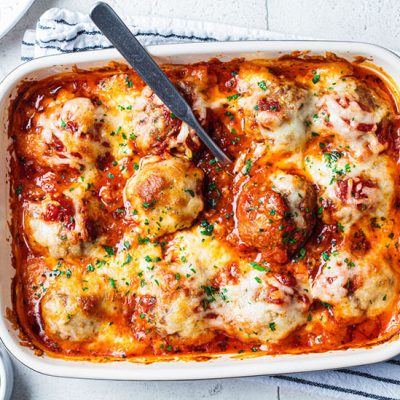 Oven baked meataballs with melted cheese in white dish with spoon on counter