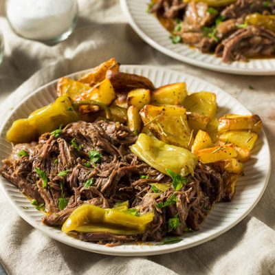 Mississippi pot roast with sliced potatoes and peppers on plate on table
