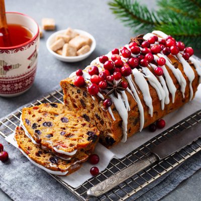 Christmas fruitcake drizzled with cream cheese frosting and berries on cooling rack