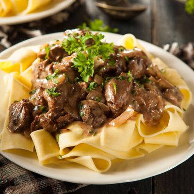 Homemade beef stroganoff with mushrooms topped with herbs on noodles