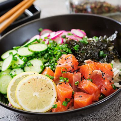 Hawaiian salmon fish poke bowl with lemon, radish, cucumber and seaweeds in bowl