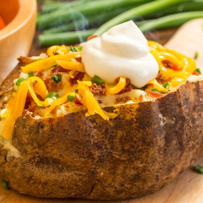 Baked potato with bacon and cheese topped with sour cream on wood board