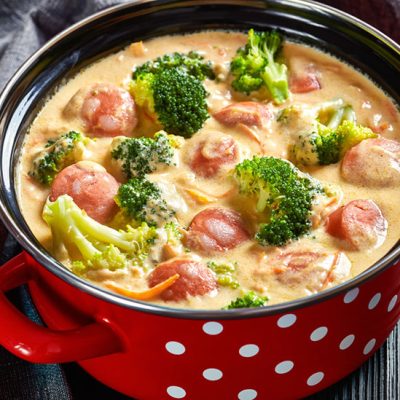 Broccoli cheddar cheese soup with sausage in red and white polka dot pot on counter