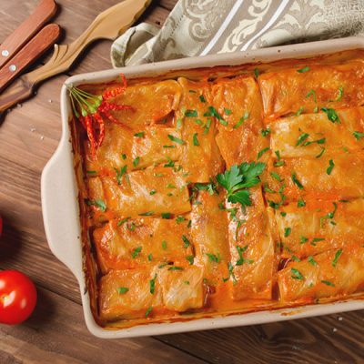 Baked cabbage rolls with tomato sauce sprinkled with chopped herbs in square dish