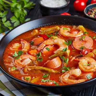 Prawn gumbo with okra and sausage in black bowl sprinkled with chopped green onions